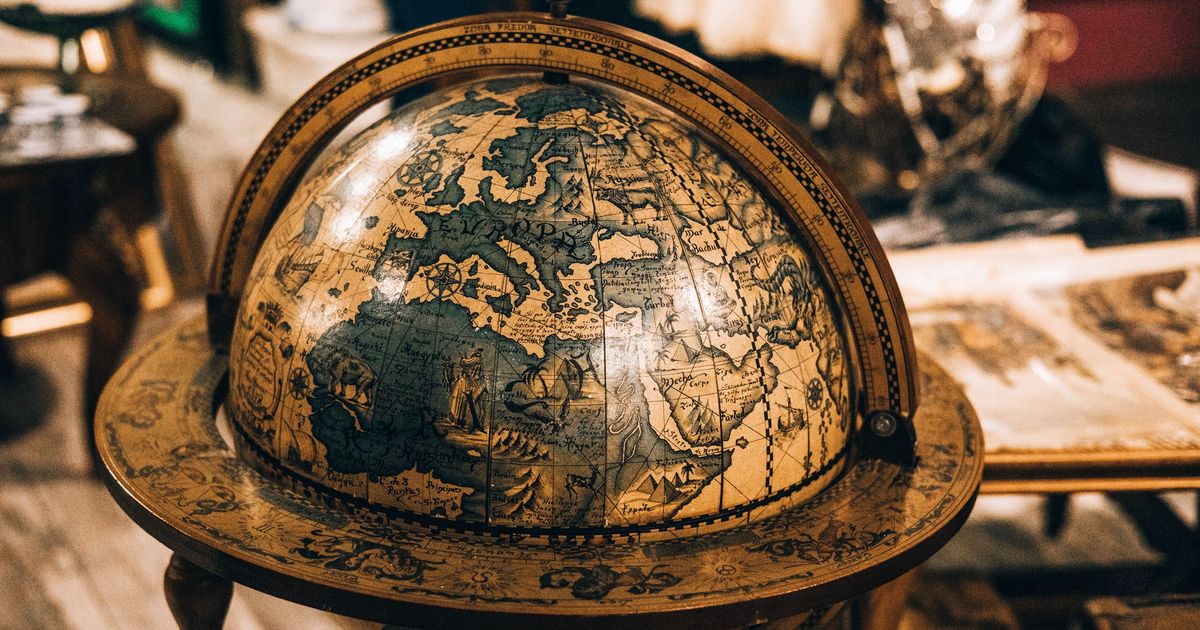 An antique globe on a wooden stand, turned to show Europe, in a warmly lit room